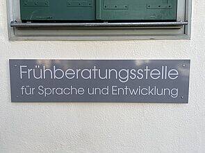 Ein Schild an einer Wand weist auf eine Frühberatungsstelle für Sprache und Entwicklung hin.