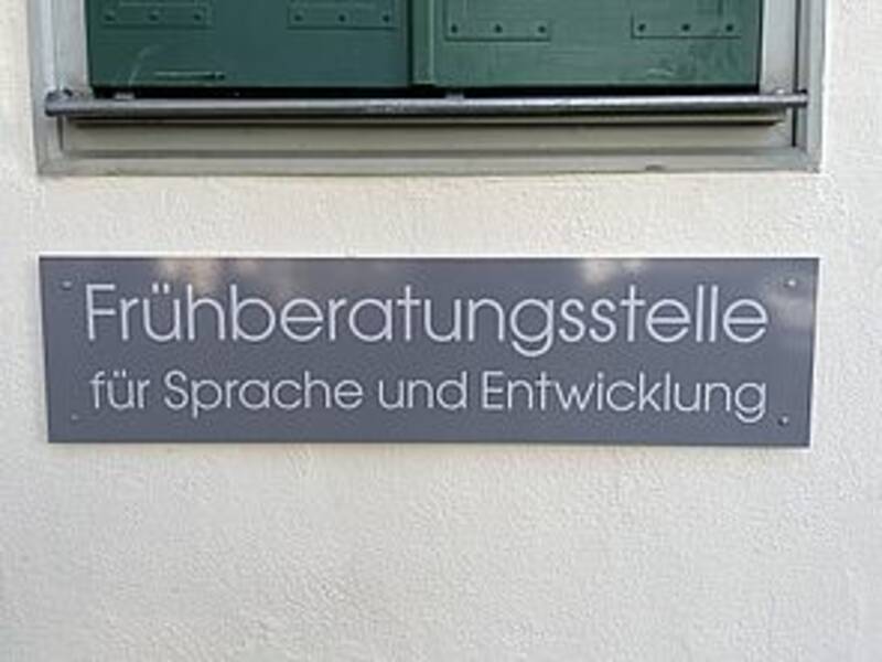 Ein Schild an einer Wand weist auf eine Frühberatungsstelle für Sprache und Entwicklung hin.