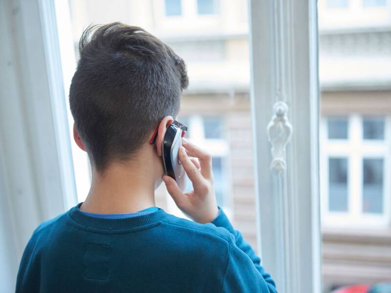 Eine Person mit kurzen Haaren telefoniert an einem Fenster, wobei nur der Hinterkopf zu sehen ist.
