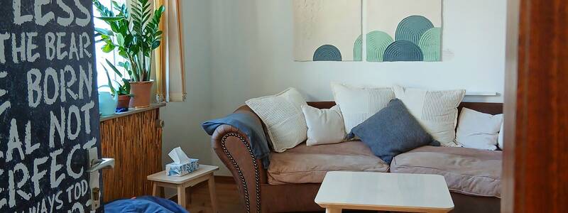 Ein gemütliches Wohnzimmer mit einer braunen Couch, mehreren Kissen, einem Holztisch, zwei blauen Sitzsäcken, dekorativen Wandbildern und einer hängenden Lampe.