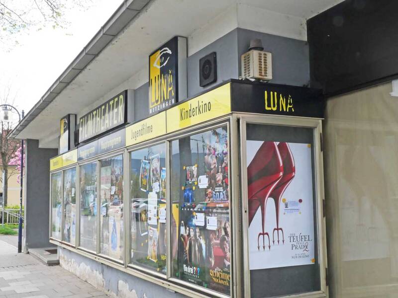 Die Außenansicht eines kleinen Kinos mit Schaufenstern voller Filmplakate und einem auffälligen Schild mit der Aufschrift "LUNA".