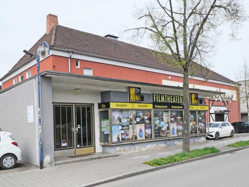 Das Bild zeigt ein kleines, rotes Kino mit der Aufschrift "Luna Filmtheater", vor dem auf einer Straße Autos geparkt sind.