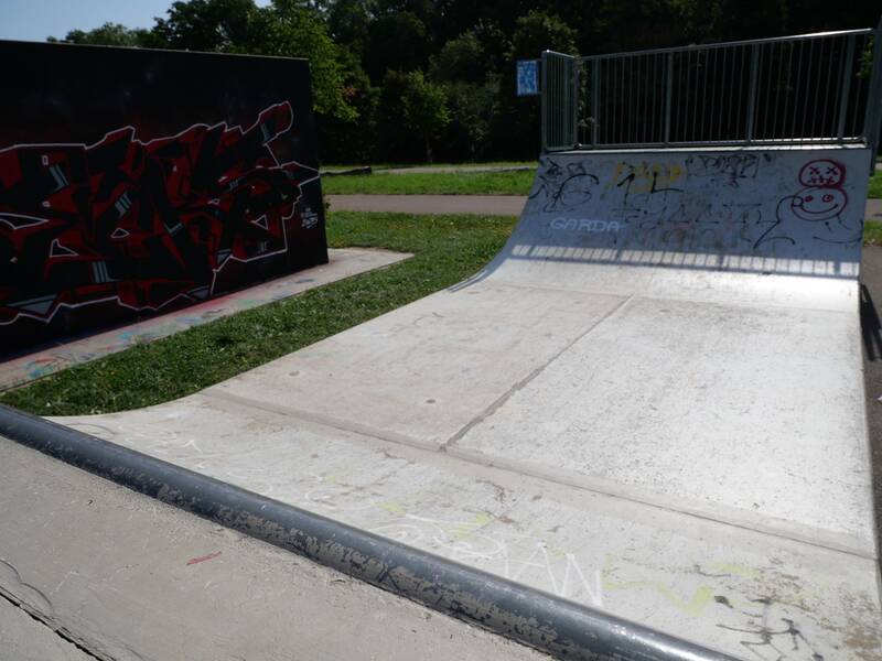 Nahaufnahme einer Halfpipe mit rotem und schwarzem Graffiti auf einer Wand daneben.