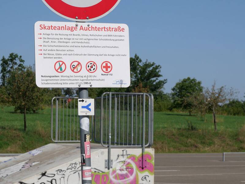Verkehrsschild mit Regeln für die Skateanlage Auchtertstraße, im Hintergrund ist eine Rampe mit Graffiti zu sehen.