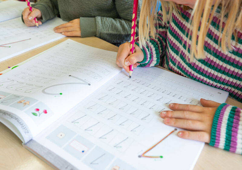 Zwei Kinder sitzen an einem Tisch und üben in Arbeitsheften das Schreiben.