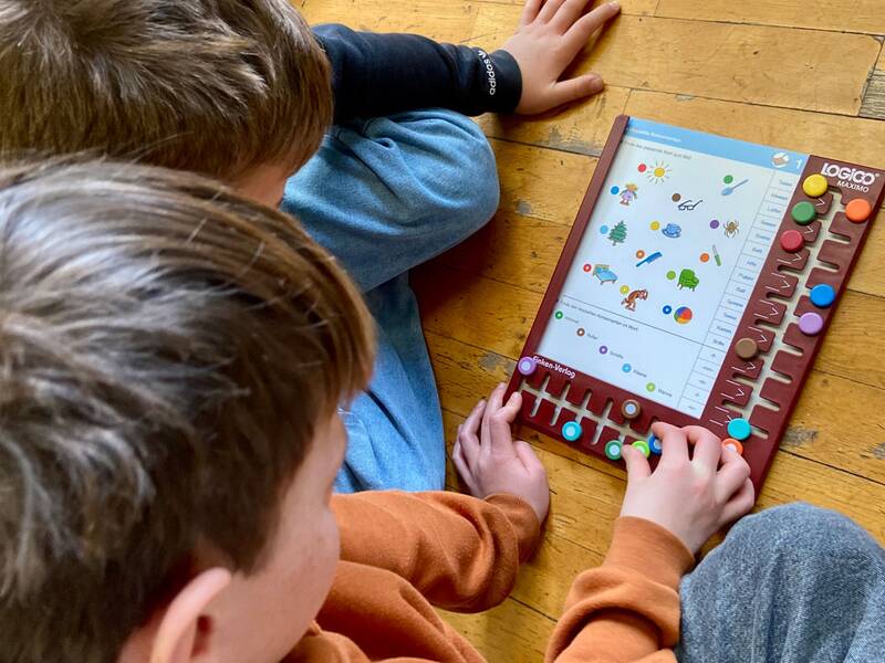 Zwei Kinder sitzen auf einem Holzboden und beschäftigen sich gemeinsam konzentriert mit einem Lernspiel mit bunten Knöpfen.