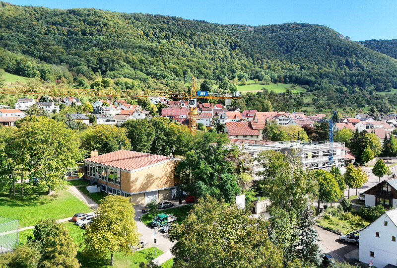 Eine malerische Kleinstadt mit roten Dächern, umgeben von üppigen grünen Bäumen und Hügeln unter einem klaren blauen Himmel.