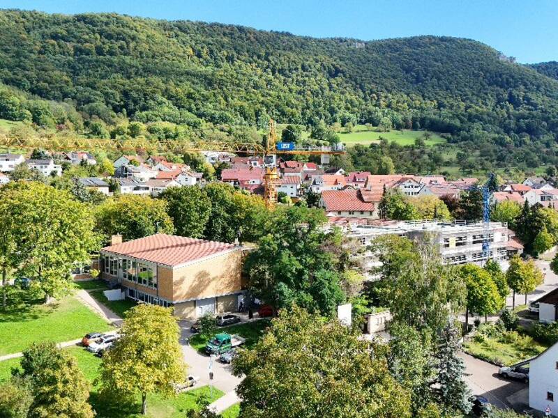 Eine malerische Kleinstadt mit roten Dächern, umgeben von üppigen grünen Bäumen und Hügeln unter einem klaren blauen Himmel.