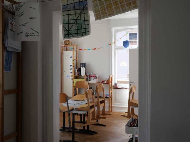 Ein heller Raum mit Holzmöbeln und bunten Papiergirlanden hängt von der Decke.