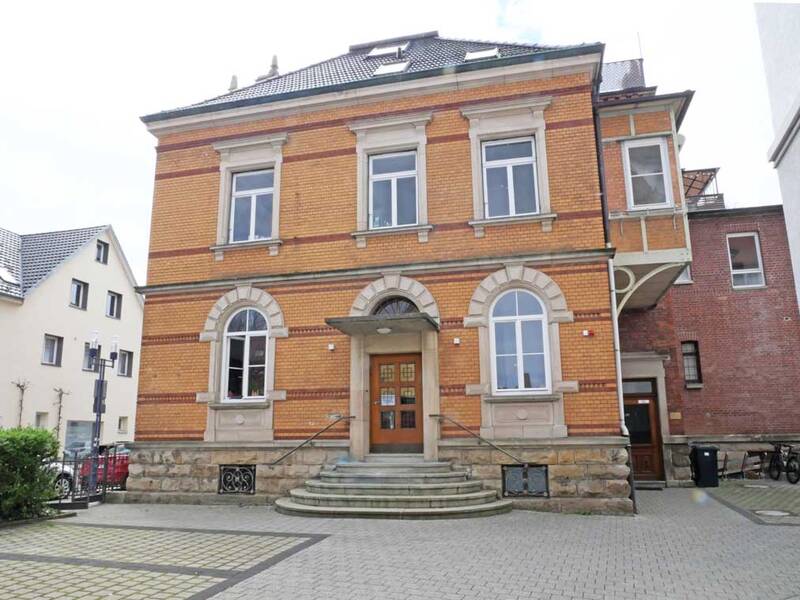Ein zweistöckiges, historisches Gebäude aus Ziegelsteinen mit Rundbogenfenstern und einer Eingangstreppe.