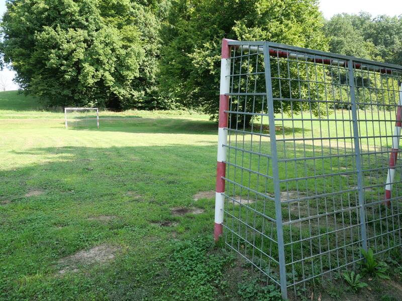 Ein Fußballplatz auf einer Wiese, im Vordergrund ein Fussballtor aus Metall.