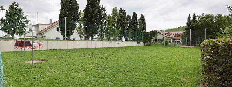 Der Bolzplatz ist von einer Mauer mit Graffiti und einem hohen Netz umgeben.