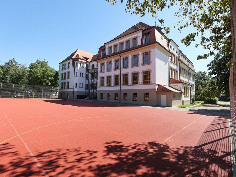 Großer roter Sportplatz vor einem Schulgebäude.