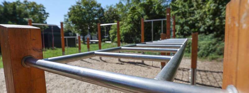 Eine Metall-Kletterstrecke mit Holzpfosten auf einem Spielplatz.