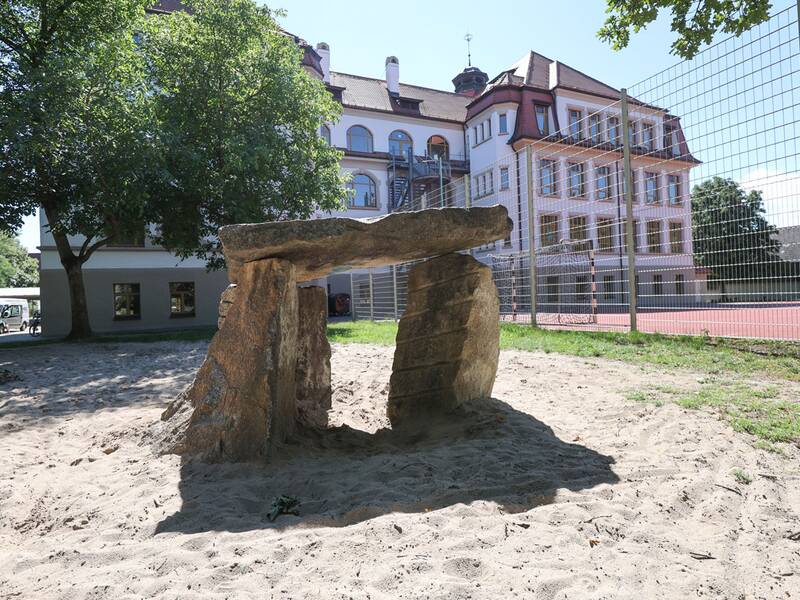 Drei große Steine im Sand bilden ein Spiel- oder Kletterelement.