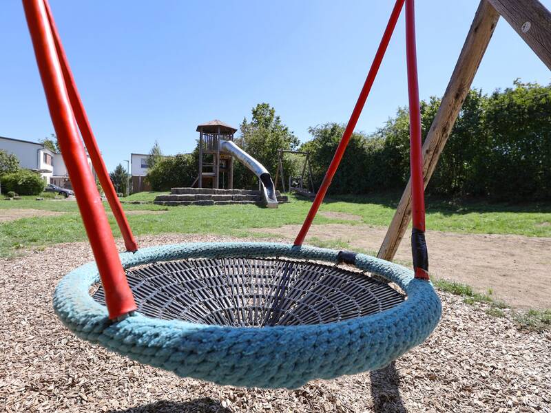 Die Nestschaukel im Vordergrund, mit Blick auf die große Rutsche und den Spielturm im Hintergrund.
