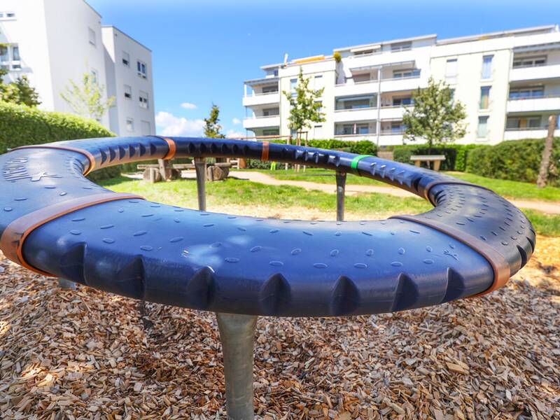 Ein rundes Klettergerät aus Kunststoff mit farbigen Markierungen steht auf Rindenmulch.