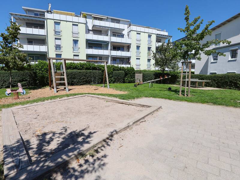 Übersicht über den Spielplatz mit Sandkasten, Rutsche, Wippe, Schaukel und Federtier.