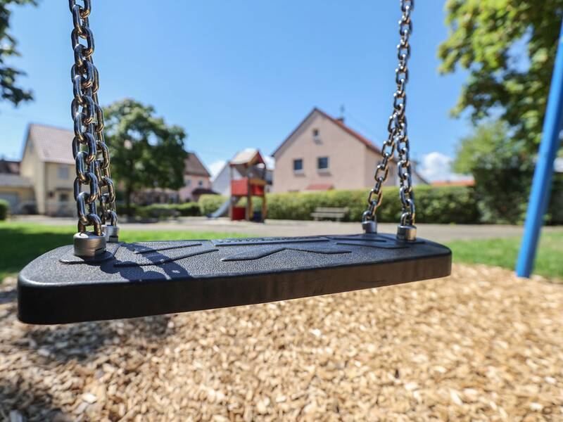 Eine leere Schaukel aus schwarzem Kunststoff über Rindenmulch.