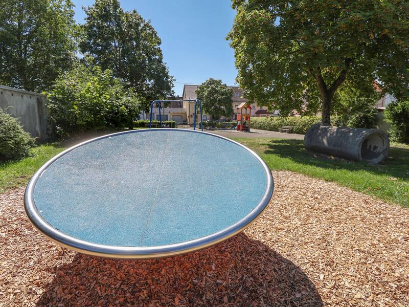 Eine große blaue Drehscheibe auf einem Spielplatz mit Rindenmulch.
