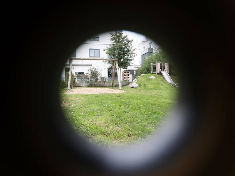 Der Spielplatz ist durch ein rundes Rohr zu sehen, im Blickfeld: Schaukel und Rutsche.