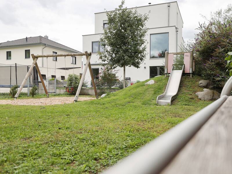 Eine kleine Rutsche führt von einem Hügel auf eine Wiese, daneben steht eine Doppelschaukel aus Holz.