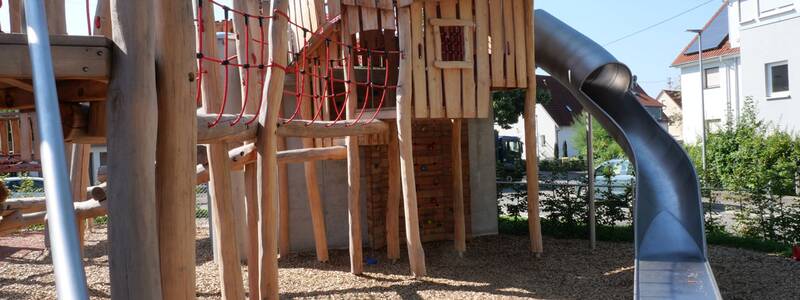 Ein moderner Kinderspielplatz mit einer Holzkonstruktion, die über Kletterelemente und eine Rutsche verfügt.