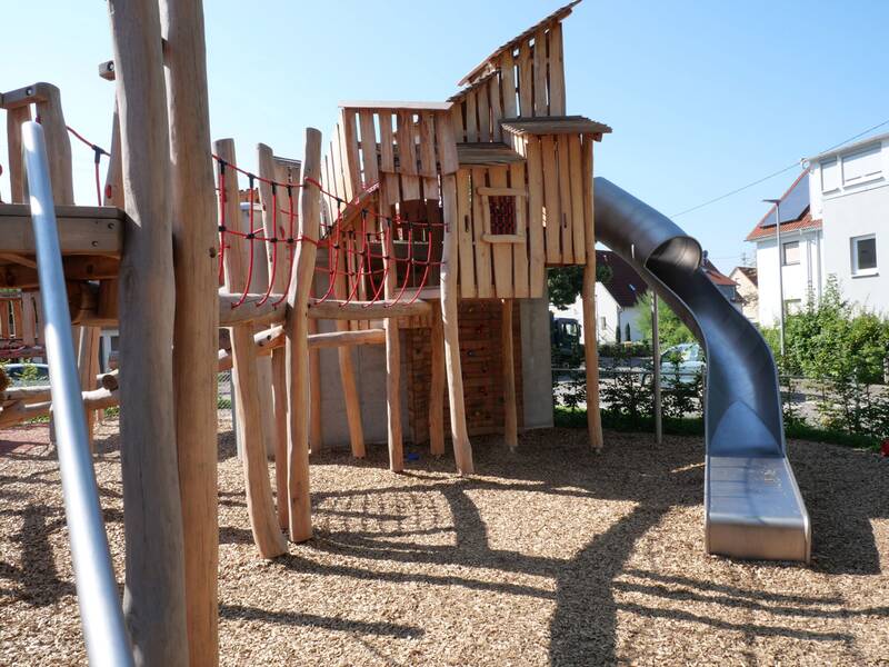 Ein moderner Kinderspielplatz mit einer Holzkonstruktion, die über Kletterelemente und eine Rutsche verfügt.