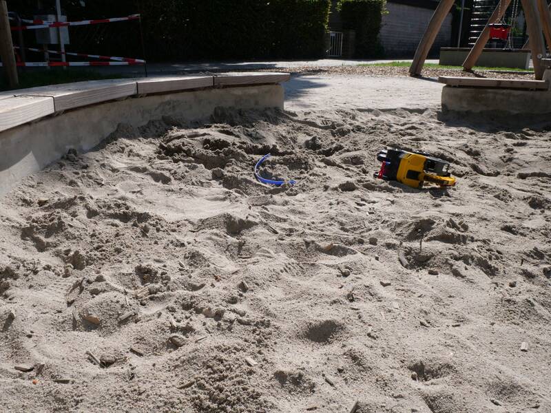 Ein Sandkasten mit einem gelben Spielzeugbagger und einer blauen Schaufel liegt in der Sonne.