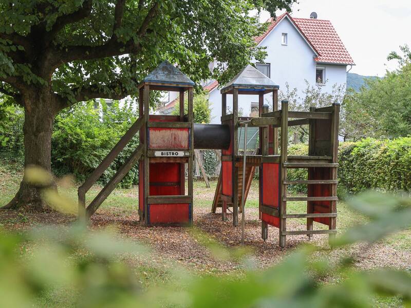 Zwei Holztürme mit roten Wänden sind durch ein schwarzes Tunnelrohr verbunden. Unter einem der Türme steht „Bistro“.