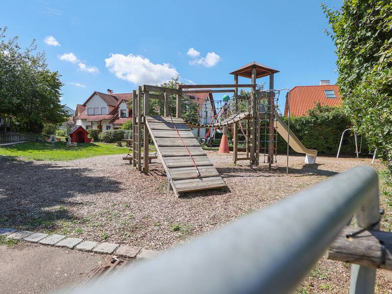 Ein großer Kletterturm mit Netzbrücken, Rutsche und Kletterwänden steht auf einem Spielplatz mit Holzhäckselboden.