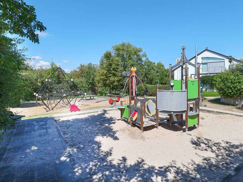 Ein Spielbereich mit Klettergerüst, Schaukelgerät und Netzpyramide auf Sand- und Rindenmulchboden.