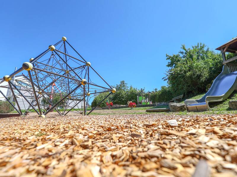 Eine große Netzpyramide auf Rindenmulch steht neben Wipptieren und einer Metallrutsche.
