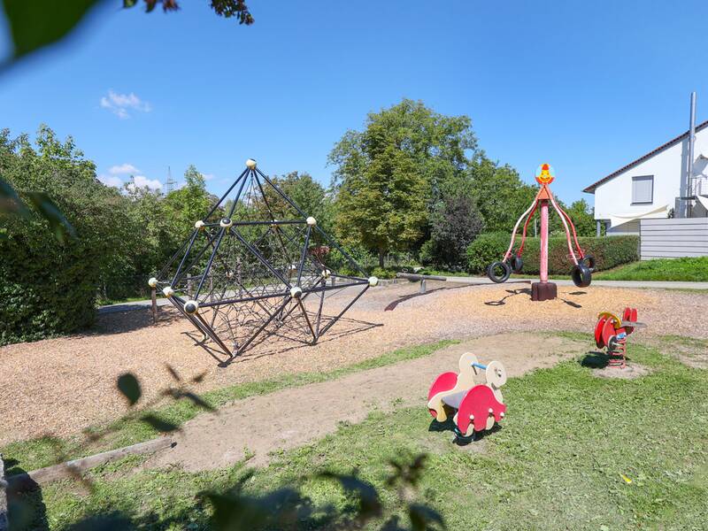 Ein Spielplatz mit Kletternetz, Wippe, Reitfiguren und einem rot-gelben Karussell aus Autoreifen.