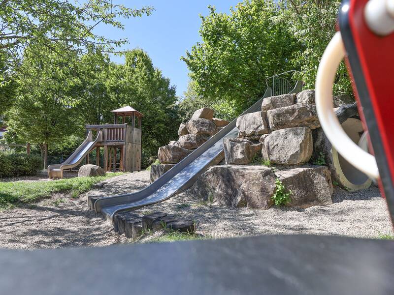 Zwei Rutschen führen von einem Felsenhügel und einem Kletterturm herunter, im Vordergrund ein Wipptier.