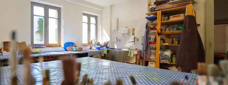 Familienzentrum Metzingen, Nahaufnahme des Tisches im Atelier mit Pinseln im Vordergrund