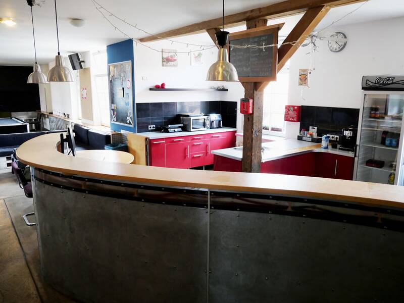Jugendhaus. Das Bild zeigt eine moderne Küche mit einer runden Theke, roten Schränken, Küchengeräten und einem kleinen Kühlschrank in einem hellen Raum.