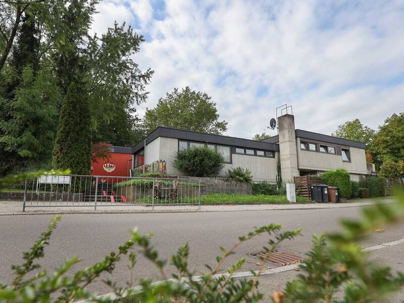 Ein modernes, einstöckiges Gebäude mit Flachdach, umgeben von viel Grün und einer Straße im Vordergrund.