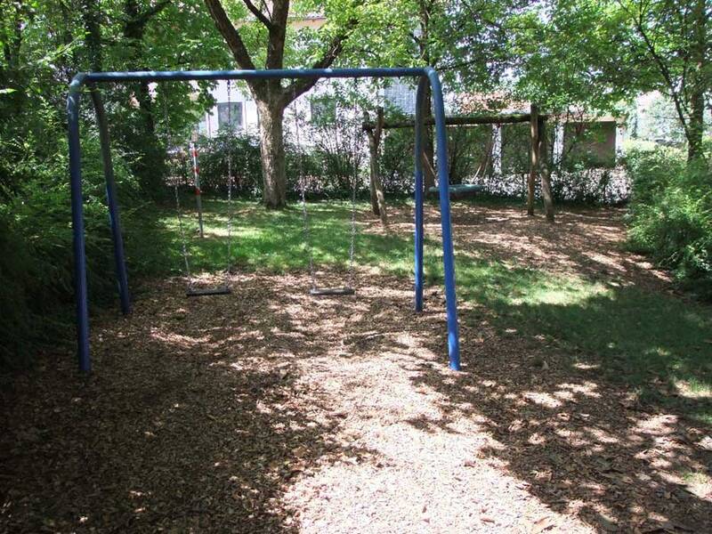 Auf dem Bild ist ein grüner Spielplatz mit zwei Schaukeln unter Bäumen zu sehen.