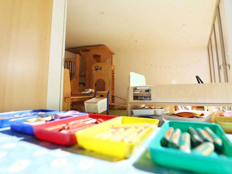 Innenansicht eines Kindergartens. Im Vordergrund sind Schalen mit Stiften in verschiedenen Farben zu sehen.