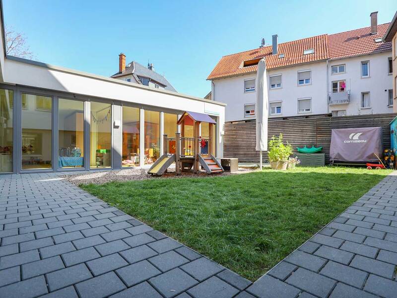 Ein Innenhof mit grünem Rasen, einem kleinen Spielplatz und umgeben von modernen Gebäuden mit großen Glasfenstern.