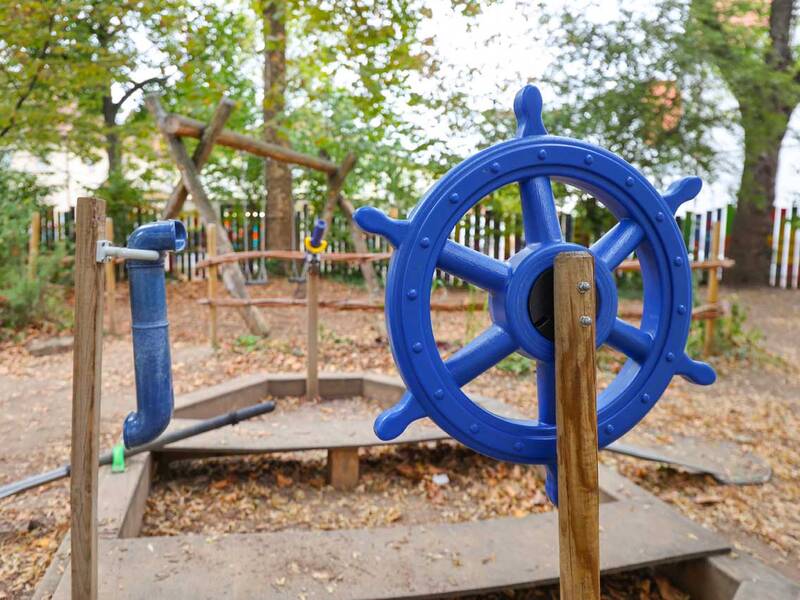 Ein blaues Steuerrad auf einem kleinen Spielplatz, umgeben von Holz und Blättern