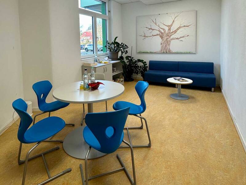 Ein helles Besprechungszimmer mit einem kleinen Tisch und vier blauen Stühlen.