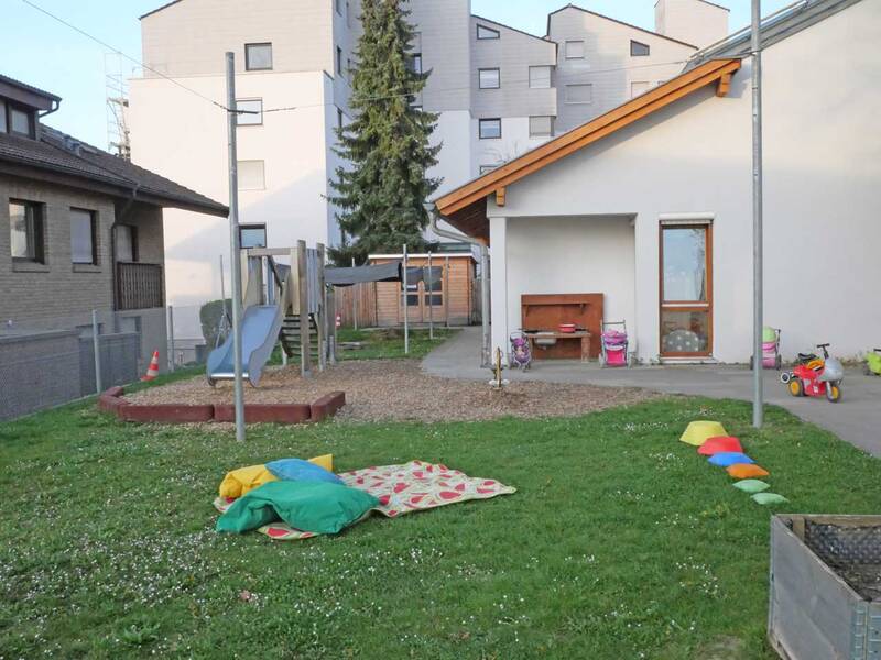 Ein Spielplatz mit Rutsche, Klettergerüst, bunten Sitzsäcken und einem Wohngebäude im Hintergrund.