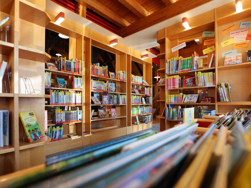 Stadtbücherei, Eine gut beleuchtete Bibliothek mit hölzernen Regalen, gefüllt mit bunten Kinderbüchern.