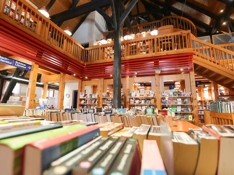 Stadtbücherei, Eine gemütliche Bibliothek mit hölzernem Interieur, zahlreichen Bücherregalen und einer Empore mit Treppe.