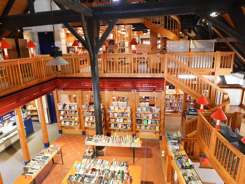 Stadtbücherei, Innenansicht einer großen, mehrstöckigen Bibliothek mit Holzbalken, Regalen voller Bücher und mehreren Leseebenen.