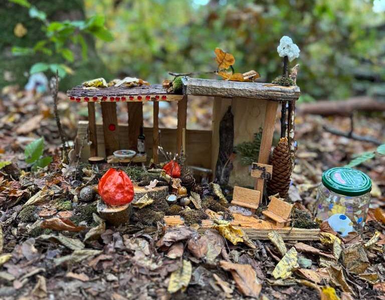 Eine kleine, aus Naturmaterialien bestehende Miniaturkulisse im Wald, umgeben von Laub und Pilzen.
