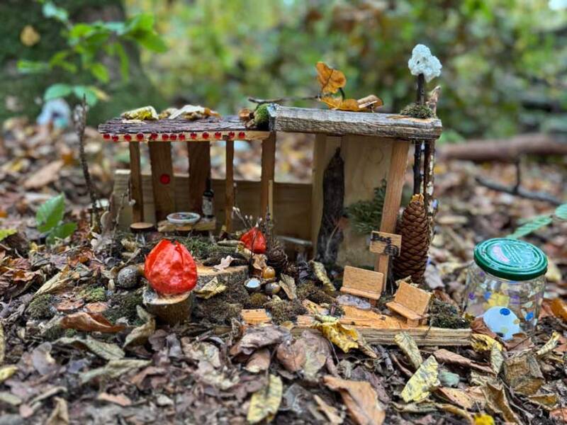 Eine kleine, aus Naturmaterialien bestehende Miniaturkulisse im Wald, umgeben von Laub und Pilzen.