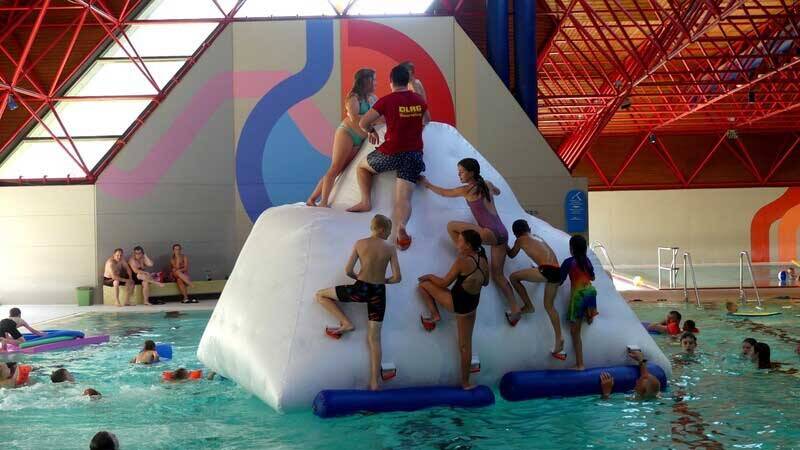 Kinder klettern auf ein aufblasbares Spielelement, das im Wasserbecken schwimmt.